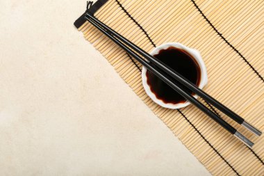 Bowl of soy sauce, chopsticks and bamboo mat on white background