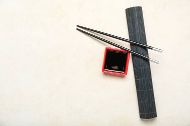 Red bowl of soy sauce, chopsticks and bamboo mat on white background