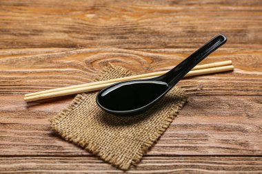 Spoon of soy sauce, chopsticks and sack cloth on wooden background