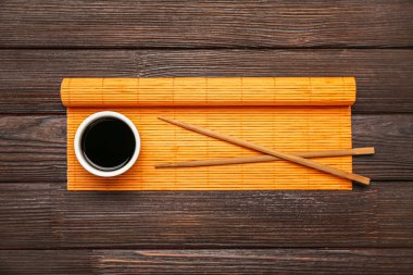 Bowl of soy sauce, chopsticks and bamboo mat on dark wooden background