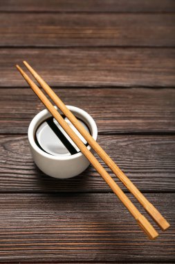 Bowl of soy sauce and chopsticks on dark wooden background