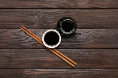Bowl and jug of soy sauce with chopsticks on dark wooden background