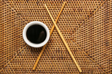 Bowl of soy sauce and chopsticks on wicker mat