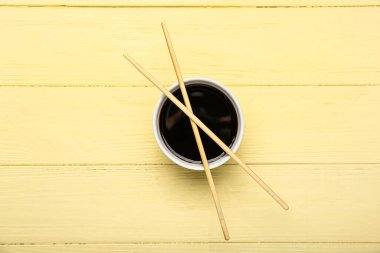 Bowl of soy sauce and chopsticks on yellow wooden background