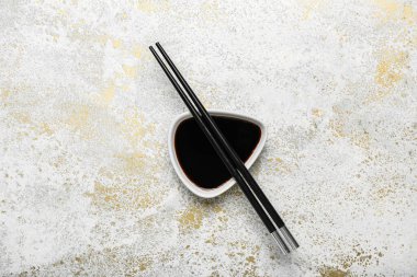 Bowl of soy sauce and chopsticks on grunge background