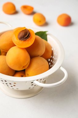 Colander full of ripe apricots on light background, closeup