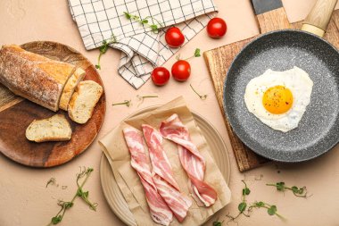 Composition with frying pan of tasty fried egg, raw bacon, bread and tomatoes on color background