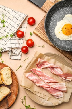Plate with slices of raw bacon, fried egg and tomatoes on color background