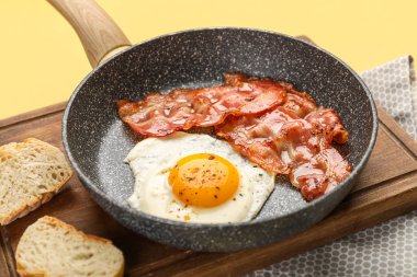 Frying pan with tasty fried egg and bacon on color background, closeup