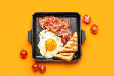 Frying pan with tasty fried egg, bacon, toasts and tomatoes on color background