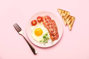 Plate with tasty fried egg, bacon and toasts on pink background