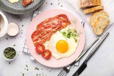 Plate of tasty fried egg with bacon and bread on light background