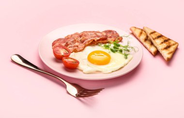 Plate with tasty fried egg, bacon and toasts on pink background