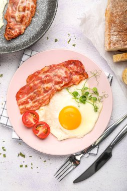 Plate of tasty fried egg with bacon on light table