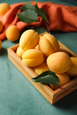 Wooden box of ripe apricots on green background, closeup