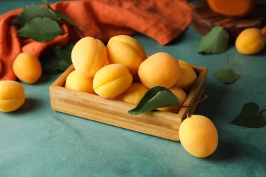 Wooden box of ripe apricots on green background