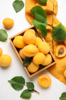 Wooden box of ripe apricots with green leaves on light background