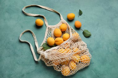 String shopping bag with ripe apricots on color background