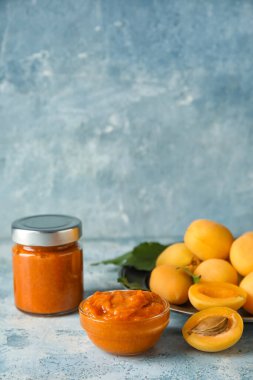 Bowl of tasty apricot jam and fruits on color background