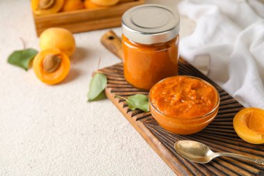 Wooden board with bowl and jar of tasty apricot jam on light table