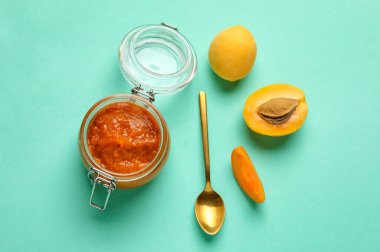Glass jar of tasty apricot jam on color background
