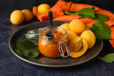 Plate with jar of sweet apricot jam and fruits on dark background