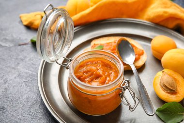 Plate with jar of tasty apricot jam on dark background, closeup