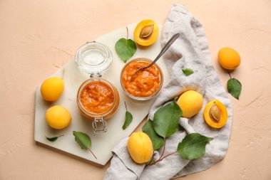 Composition with jar of tasty apricot jam, fruits and green leaves on color background