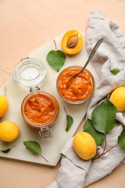 Composition with jar of tasty apricot jam, fruits and green leaves on color background