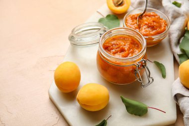 Board with jar of tasty apricot jam on color background