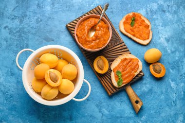 Composition with bowl of apricot jam, sandwiches and fruits on color background