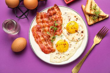 Plate of tasty fried eggs with bacon, spices and toasts on color background
