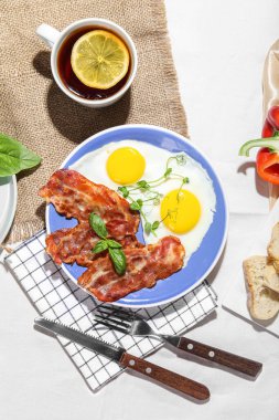 Plate with tasty fried eggs, bacon and cup of tea on table