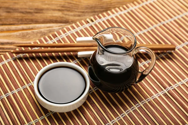 Bowl and jug of soy sauce with chopsticks on bamboo mat, closeup