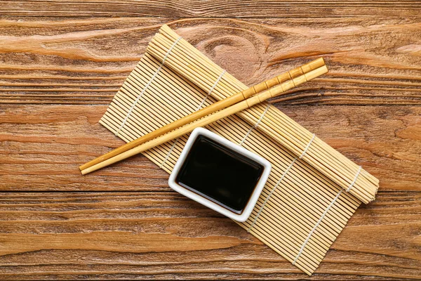 stock image Bowl of soy sauce, chopsticks and bamboo mat on wooden background