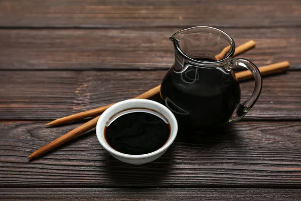 Bowl and jug of soy sauce with chopsticks on dark wooden background