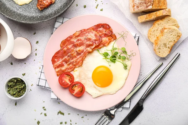 Plate of tasty fried egg with bacon and bread on light background
