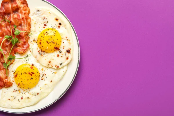 Plate of tasty fried eggs with bacon and spices on color background