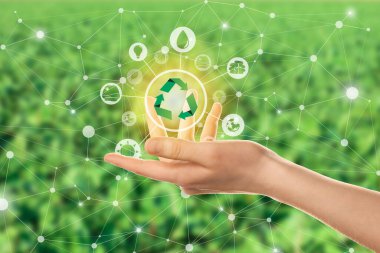 Female hand with digital icons and recycling symbol on blurred green background. Concept of green technology