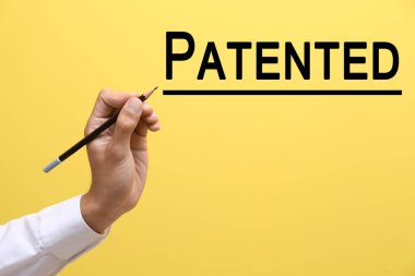 Male hand with pencil and word PATENTED on yellow background