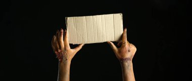 Hands of zombie with blank cardboard sheet on dark background. Halloween concept