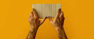 Hands of zombie with blank cardboard sheet on yellow background. Halloween concept