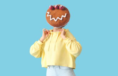 Woman with funny monster cookie instead of her head on light blue background. Halloween celebration