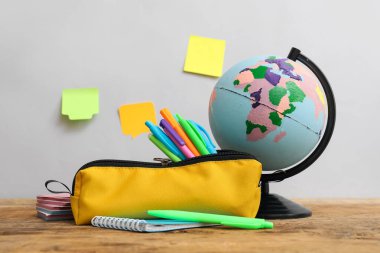 Yellow pencil case with school stationery and globe on table against grey background