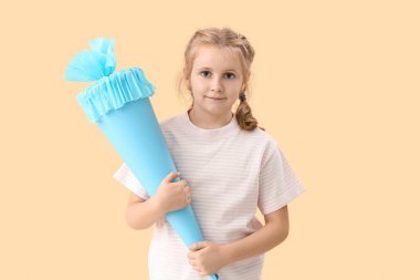 Cute little girl with blue school cone on beige background