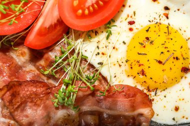 Tasty fried egg, bacon and tomatoes with spices, closeup