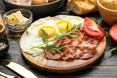 Plate of tasty fried eggs with bacon on dark wooden table, closeup