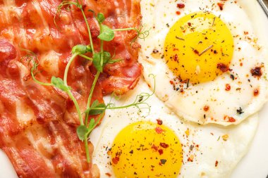 Tasty fried eggs with bacon and spices, closeup