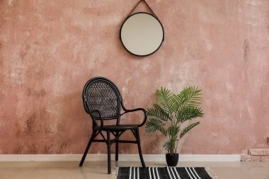 Stylish chair, houseplant and mirror hanging on pink wall