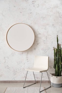Stylish chair, cactus and mirror hanging on light wall